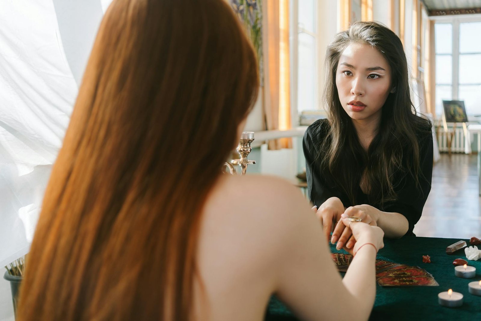 A serene tarot card reading session between two women, with candles and crystals around them, creating a mystical atmosphere.