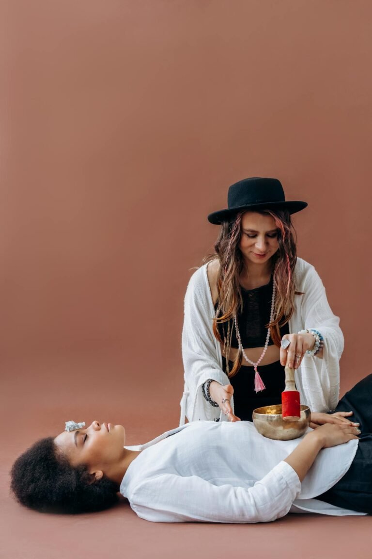 Woman practicing sound healing with a Tibetan singing bowl on a relaxing client indoors.